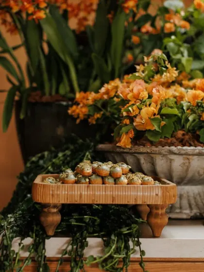 Small bites are presented on rustic wooden platters, surrounded by potted plants and cascading greenery. This thoughtful presentation integrates the catering with the overall garden theme.