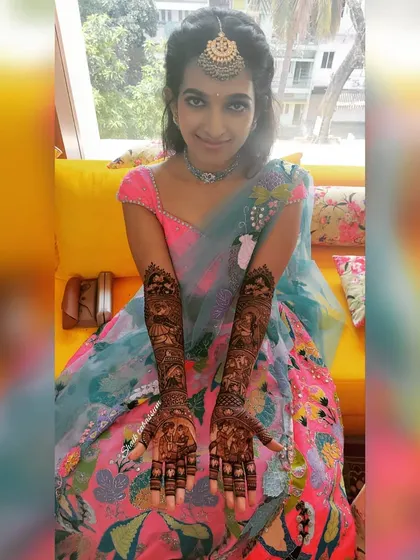 A beautiful bride proudly displaying her full bridal mehendi. The dark stain of the henna contrasts beautifully with her colorful lehenga, completing her festive look.