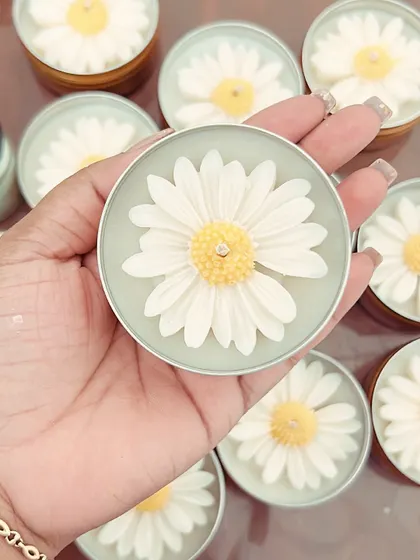 Holding a daisy tin candle to show its size. It's a perfect, cute, and budget-friendly option for those new to scented candles.