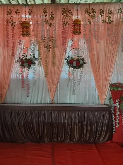 A stage backdrop with peach drapes and hanging floral elements. This can be set up for various functions like engagements or religious events.