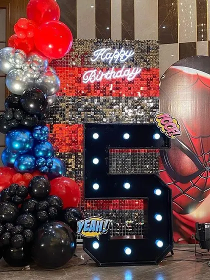 A close-up of the Spider-Man setup, showing the large light-up number '5', a silver sequin wall, and a giant inflatable Spider-Man head.