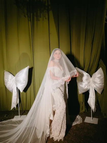 The bride, a vision in her veiled gown, standing beside oversized satin bows that were a signature element of her reception decor.