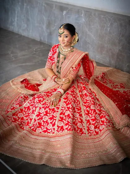 A magnificent wide shot showcasing the grandeur of the bride's lehenga. The makeup is kept soft and radiant to balance the opulence of her attire, creating a look of pure grace.