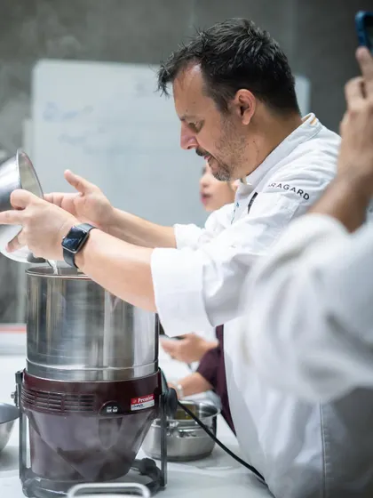 A student gets hands-on experience, adding cacao nibs to the grinder during the bean-to-bar chocolate workshop with Chef Olivier Fernandez.