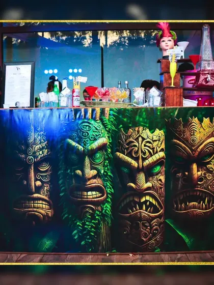 A custom-designed Tiki bar front that instantly transports guests to a tropical paradise. The detailed, expressive faces create a powerful visual anchor for the event's theme.