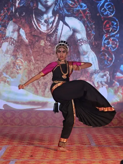 A student performs a dynamic kick in front of a backdrop of Lord Shiva, embodying the energy of the cosmic dancer.