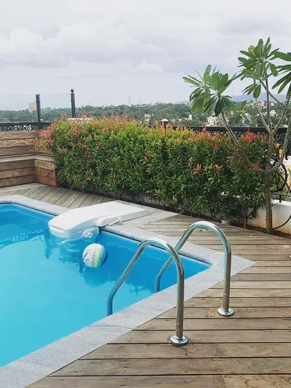 This view highlights the details of a residential terrace pool deck we designed in Mysore. The rich wooden decking is complemented by a privacy hedge of red-tipped photinia, adding color and seclusion to this private oasis.