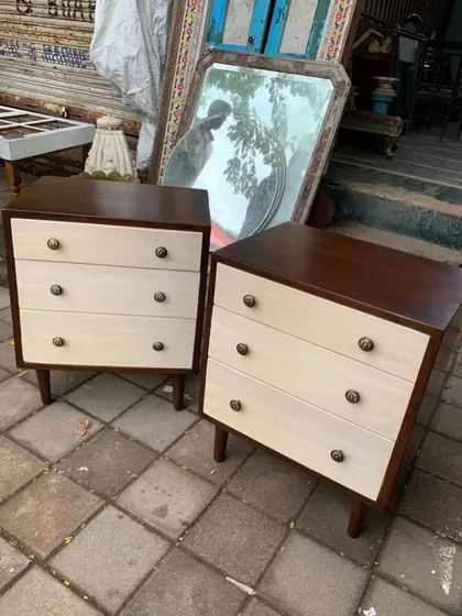 A pair of mid-century style bedside tables or small chests of drawers. They feature a two-tone finish with a dark teak frame and light-colored drawer fronts with antique-style knobs.