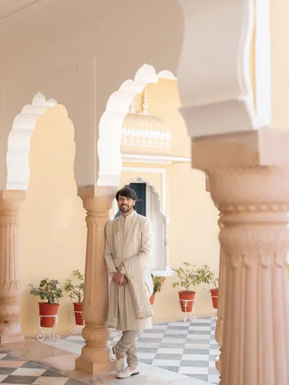 A relaxed portrait of the groom leaning against a pillar in a sunlit palace corridor, his calm demeanor a contrast to the wedding day excitement.