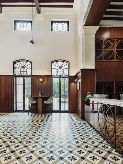 The bar area at The Bangalore Club features tall, arched windows that flood the space with light. We designed a mirrored bar front that reflects the classic black and white floor tiles, adding a touch of modern glamour to the historic setting.