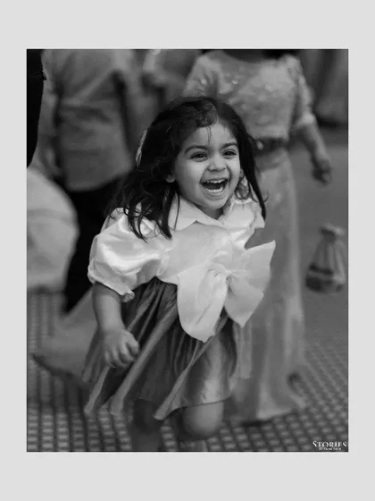 A candid black and white photo of a young girl running and laughing, capturing the joyful and carefree spirit of a wedding.