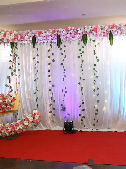 A popular rental for naming ceremonies is this floral crescent moon swing, providing a unique photo opportunity and seating element against a simple white curtain backdrop with fairy lights.