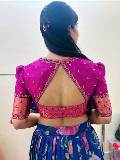 A back view of a client's blouse, featuring puffed sleeves and a triangular keyhole cut-out in a vibrant pink brocade fabric.