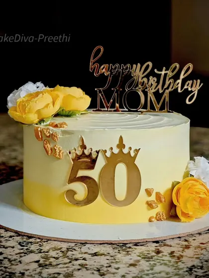 A sunny and cheerful cake for a mom's 50th birthday. The yellow ombre buttercream is decorated with golden accents, a custom topper, and beautiful yellow and white sugar flowers.