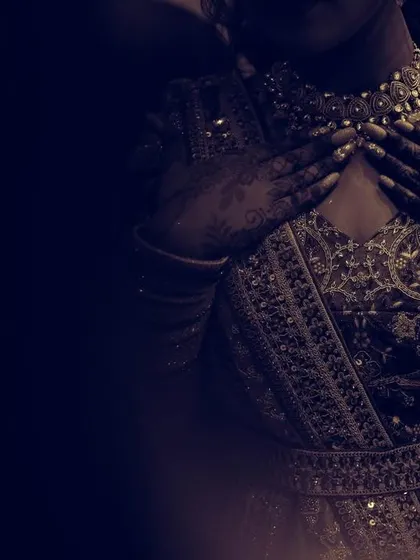 A close-up, artistic shot focusing on the intricate details of the bride's outfit and henna-adorned hands.