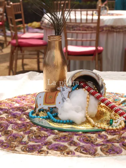 A table centerpiece for the Krishna party. It included a miniature cow figure, a peacock feather in a golden bottle, and traditional beaded jewelry, capturing the essence of the theme.