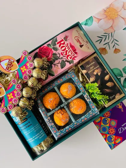 We can customize the contents of the same box. This version of the floral box includes laddoo-shaped candles and Shubh Labh hangings.