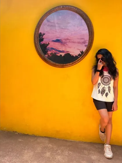 A casual pose against a vibrant yellow wall, with a dreamcatcher shirt. This image has a bohemian, artistic vibe perfect for lifestyle content.