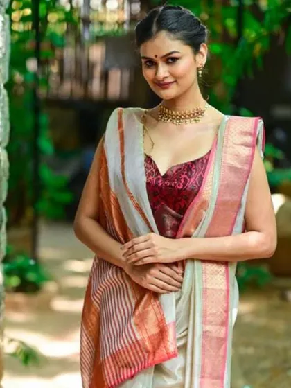 A model wears a simple gold choker that perfectly complements the rich gold border of her linen saree.