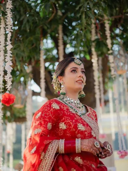 A beautiful portrait of the bride under a tree adorned with floral hangings, looking up with a hopeful and serene expression.
