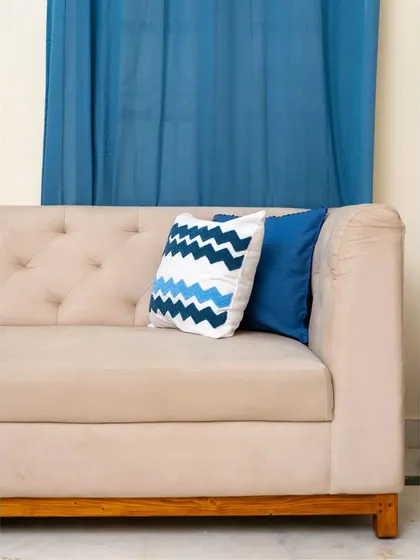A close-up of the tufted sofa, showcasing the fabric texture and the decorative cushions that add a pop of color and pattern. The wooden base provides a warm, natural contrast to the soft upholstery.