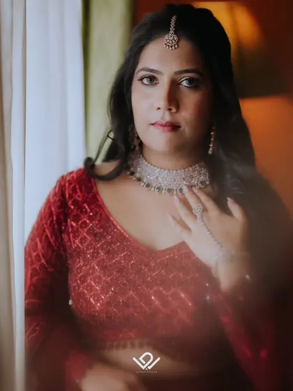 A close-up portrait of a bride in a red lehenga, her thoughtful expression captured in soft light.