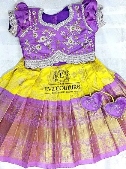 A newborn pattu lehenga with cute "Baby Sis" heart tassels. This yellow and purple set is perfect for a baby sister's first big event.