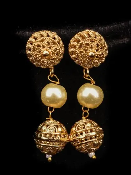 A pair of gold-toned drop earrings with intricate filigree spheres and pearl accents. This design has a vintage feel and adds a touch of sophisticated charm.