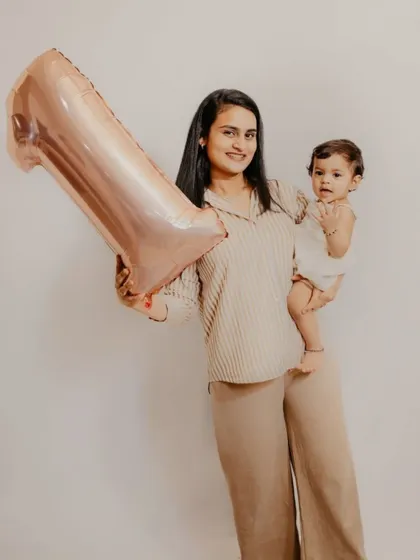 A proud mother holds her baby and a "1" balloon to celebrate her child's first birthday milestone.