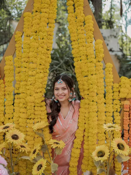 The bride peeks through a curtain of marigolds with a playful smile.