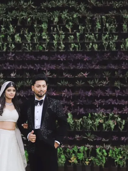 A modern, chic portrait of a couple against a living wall of green and purple foliage. The contrast between their formal wear and the natural texture creates a visually striking image.