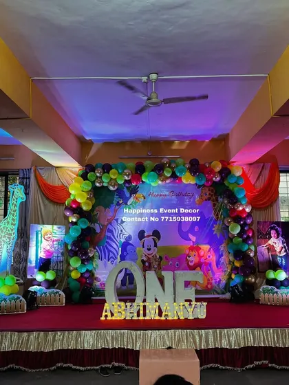 A vibrant jungle-themed birthday stage with light-up animal props like a giraffe and elephant. The decor also includes a large 'ONE' sign and the child's name in marquee letters.