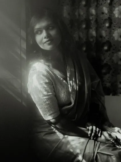 A classic black and white window-lit portrait. The play of light and shadow across the model's face and clothing creates a timeless, cinematic feel, full of quiet contemplation.