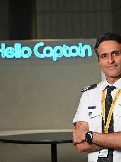 A confident, crossed-arm pose of a pilot. The on-location setting at the IndiGo office adds an authentic corporate feel.