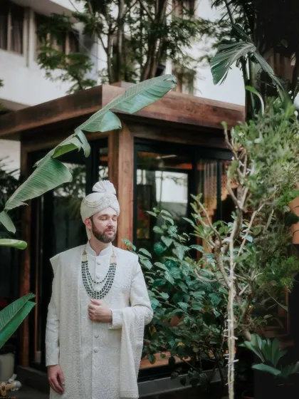 A portrait of the groom, looking dapper and ready for the ceremony. His elegant white sherwani and the lush green background create a fresh and sophisticated look.