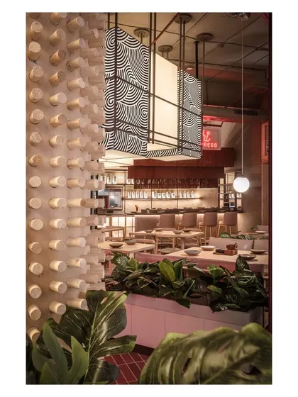 A textured wooden dowel wall adds a unique tactile element to the space, contrasting with the sleek bar and lush plants. This detail demonstrates our focus on materiality to create a rich sensory experience.