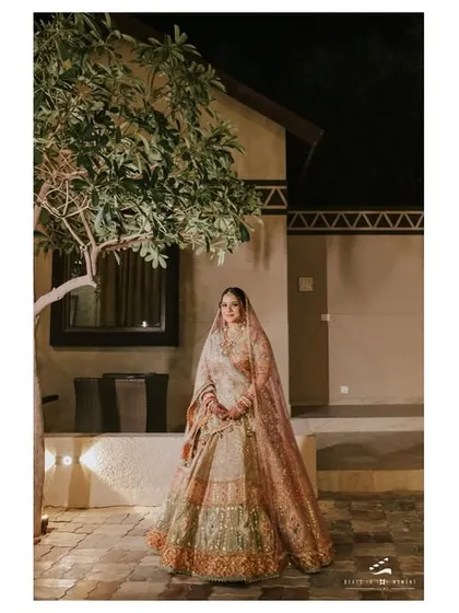 A full-length shot of the bride in her gorgeous lehenga, set against a modern, elegant backdrop. This portrait showcases her complete look with grace.