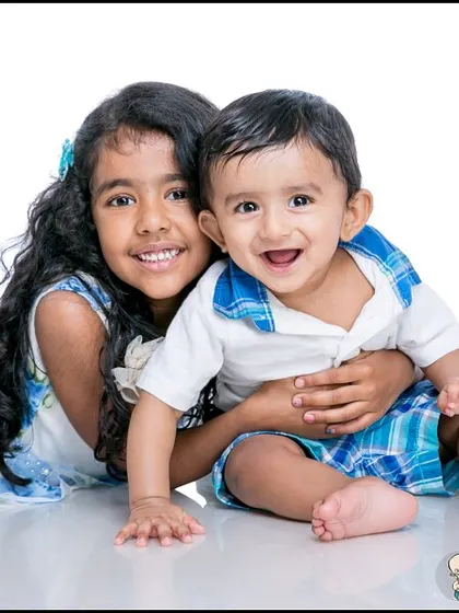 A classic studio portrait of an older sister hugging her baby brother. Their happy smiles and the simple white background create a timeless and heartwarming sibling photo.