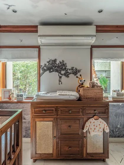 A full view of the changing area. The wooden dresser with cane details provides ample storage, and the space is framed by two large windows that let in beautiful natural light.
