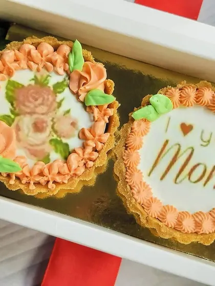 A detailed close-up of the two mini chocolate tarts, focusing on the delicate floral print and the heartfelt message for Mom.