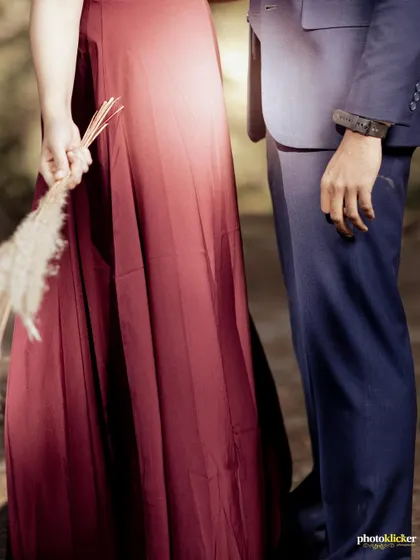 A close-up detail shot of a couple's hands and attire, with the woman holding dried pampas grass, set against a forest background.