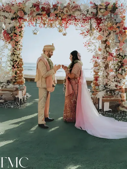 A beautiful moment from a beachside wedding. The couple stands under a floral arch, exchanging rings with the ocean waves in the background, a perfect destination wedding shot.