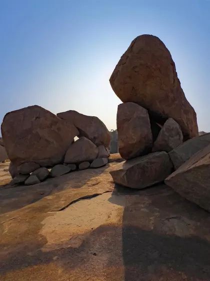 The sun backlights a formation of giant boulders, creating strong silhouettes and shadows. This shot highlights the dramatic and almost otherworldly geology of the area.
