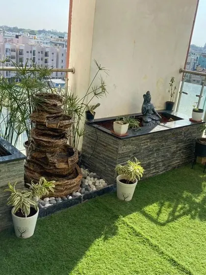 A compact water feature and a stone-clad planter with a built-in pond bring the soothing sounds of water to this balcony. The space is designed for tranquility, featuring a Shiva statue and bamboo plants.