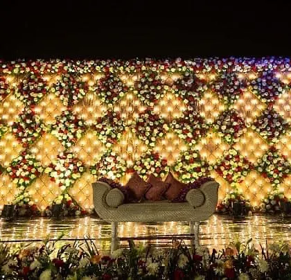 A truly grand wedding stage I created, featuring a massive wall of fresh flowers arranged in a diamond pattern with integrated lighting. This kind of opulent backdrop makes for stunning photographs and leaves a lasting impression on guests.