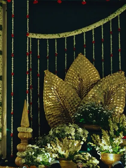 A close up of a traditional decor element, featuring golden palm leaves against a dark backdrop with hanging jasmine garlands. This highlights our ability to blend elegance with tradition in every detail.