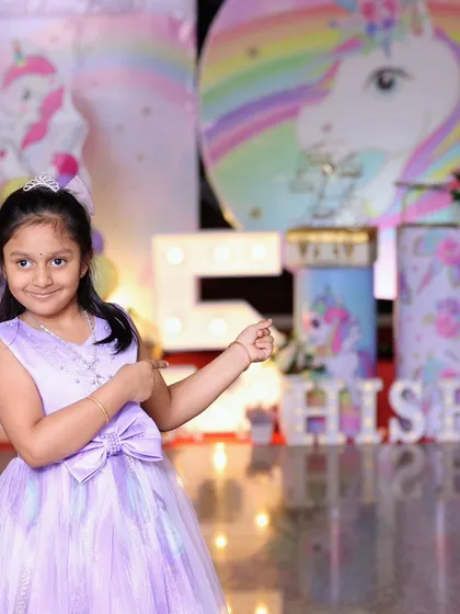 The birthday girl posing proudly at her unicorn-themed party. Her dress even matches the pastel decor!
