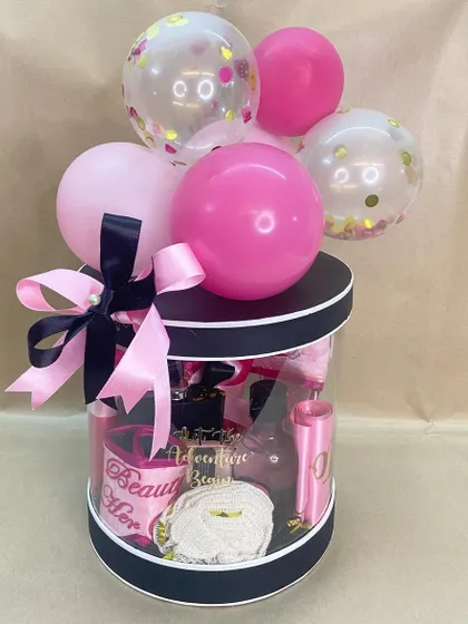 A 'Bride To Be' hamper from her bride tribe. This clear cylindrical box is filled with pink and black themed goodies and topped with a balloon bouquet.