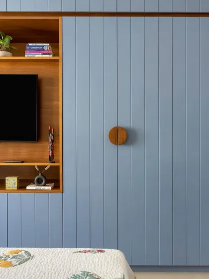 This bedroom features a fully paneled wall in a calming blue, with an integrated TV unit and custom circular wooden handles on the wardrobe.