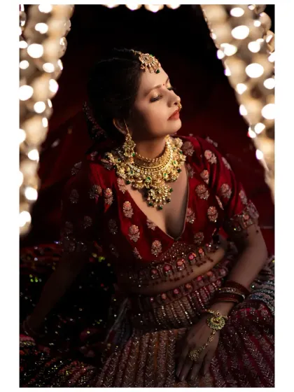 A dramatic bridal portrait using warm, focused light. The bride, in a rich red lehenga, looks absolutely radiant and serene.